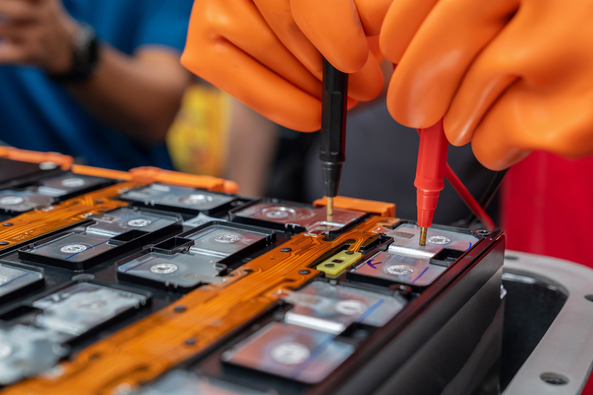 Neatly arranged LFP batteries wired to a control board in an EV. Technician uses a voltage tester while wearing safety gloves, emphasizing innovation, rechargeable battery safety, and environmental conservation.