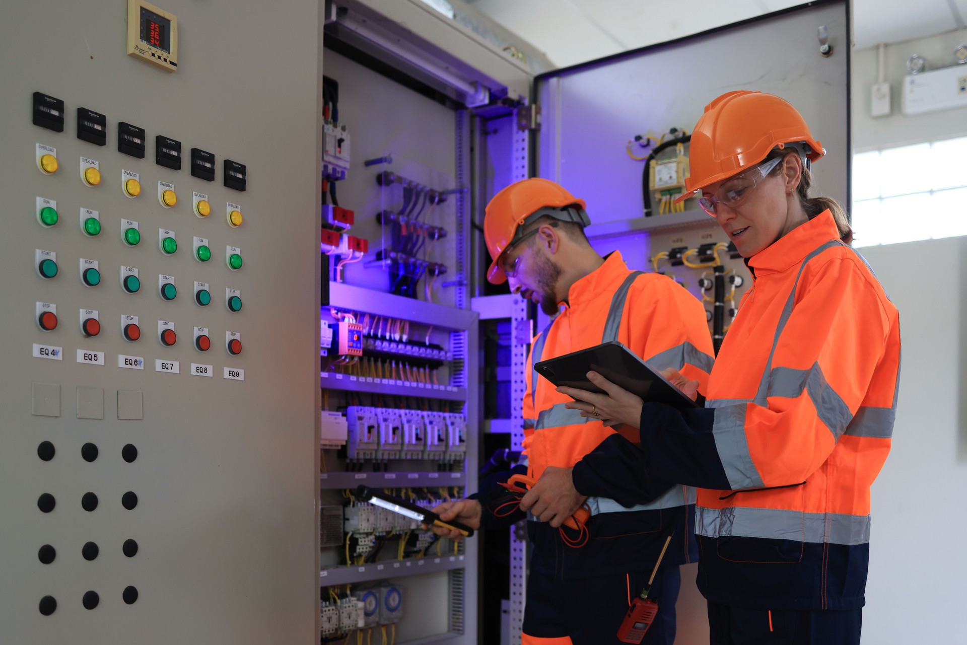 Engineering Motherhood: Expectant Female Engineer and Male Colleague with an orange safety suit  in the Electric Control Room MDB Main Distribution Board