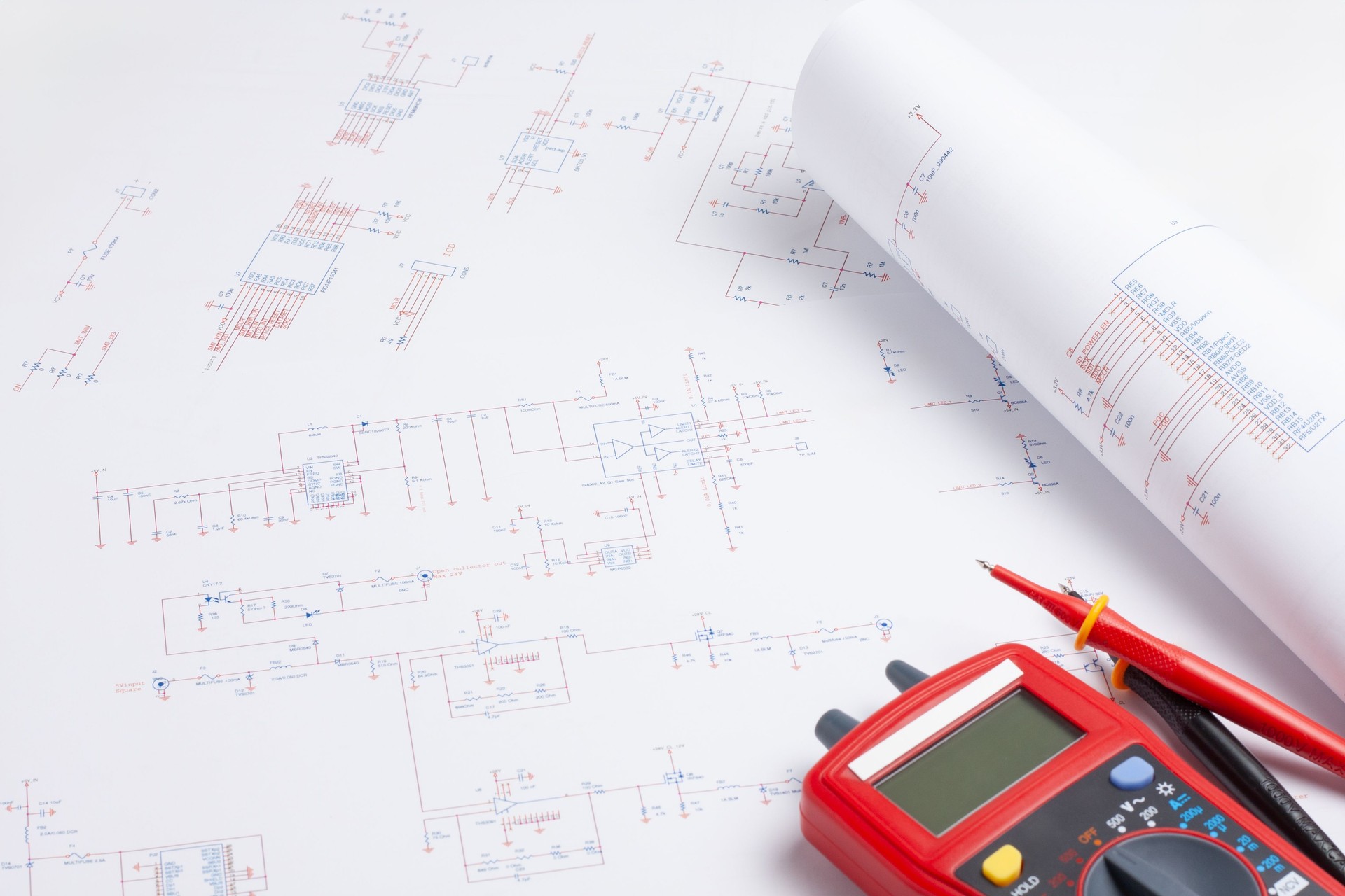 Engineer's desk with multimeter and a rolled bluepint.