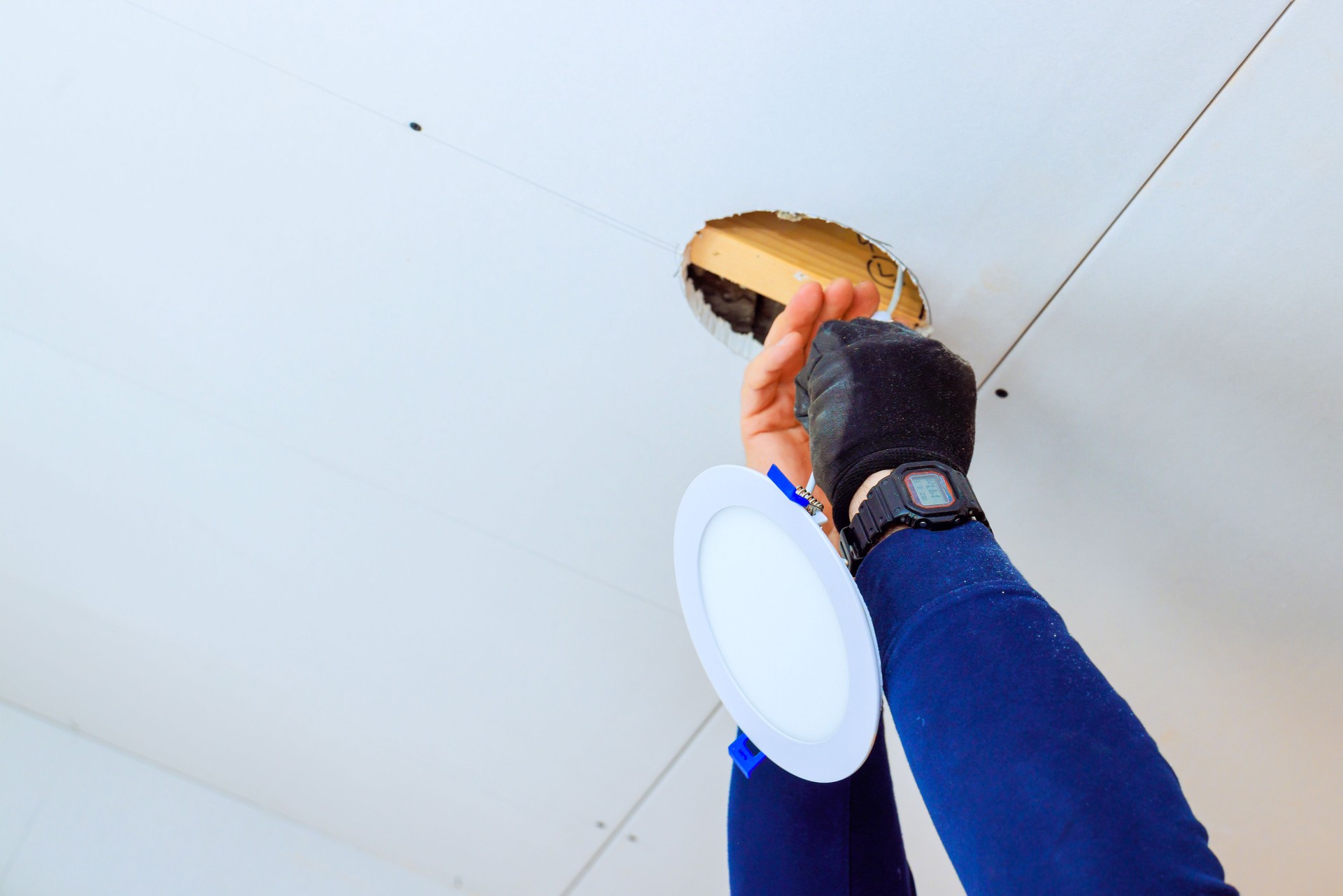 Worker installs lighting fixture in ceiling during home renovation project in modern interior space